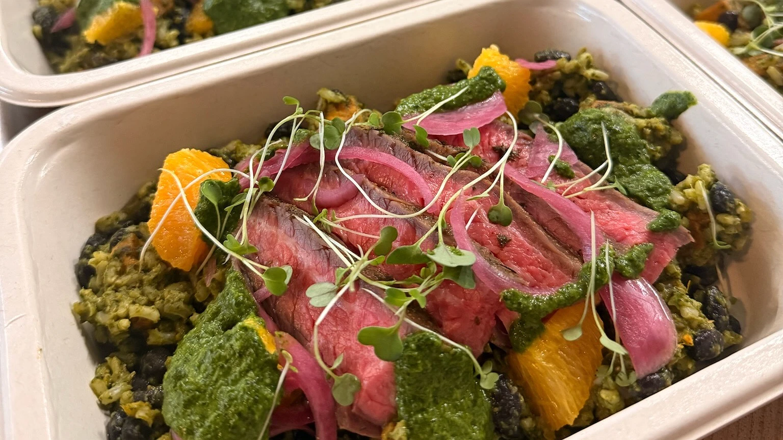 Grain bowl with sliced steak, orange, pickled red onion and herb sauce, packed to go
